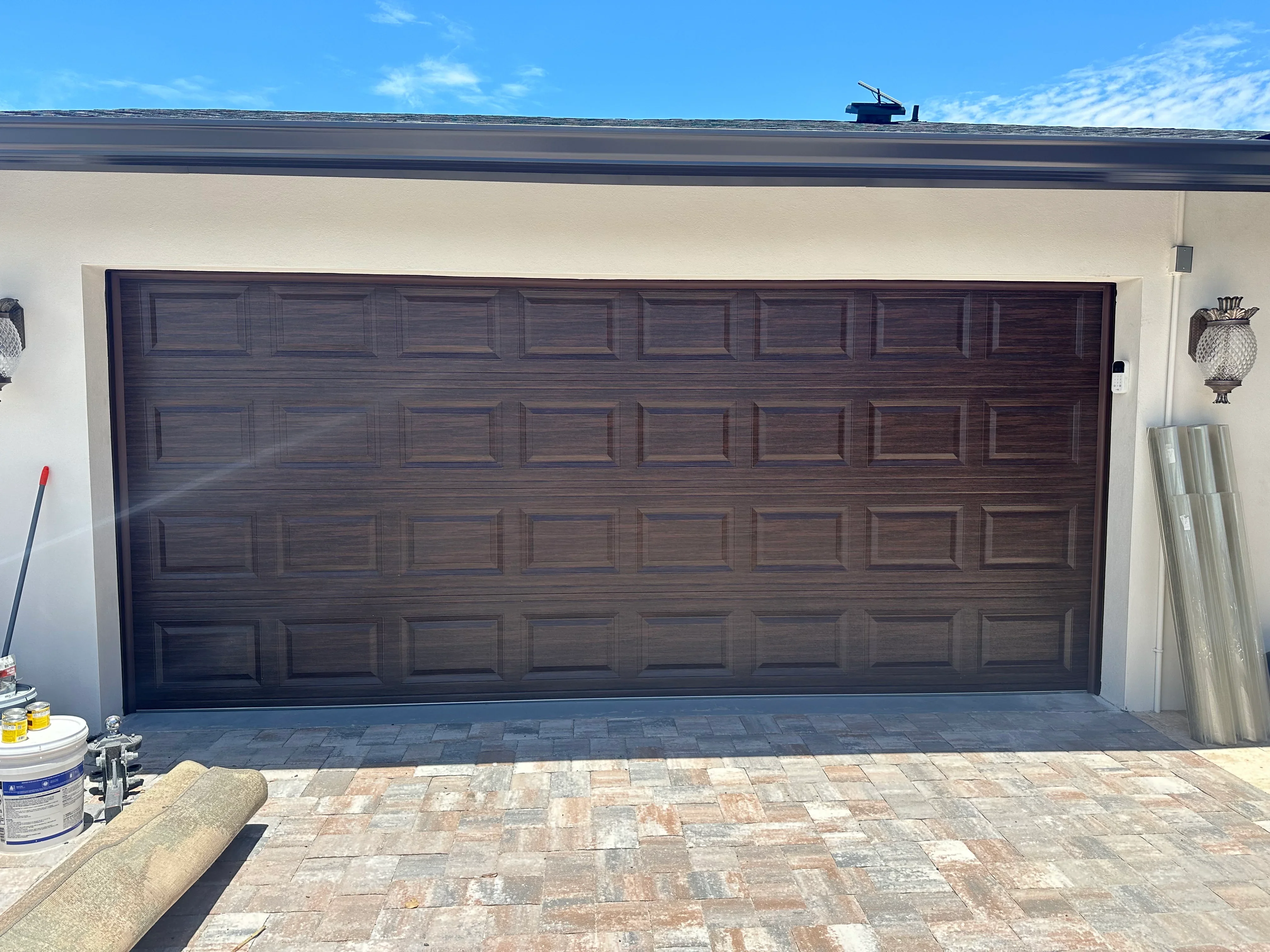 Dark wood grain 16-panel garage door on cream garage with paver driveway