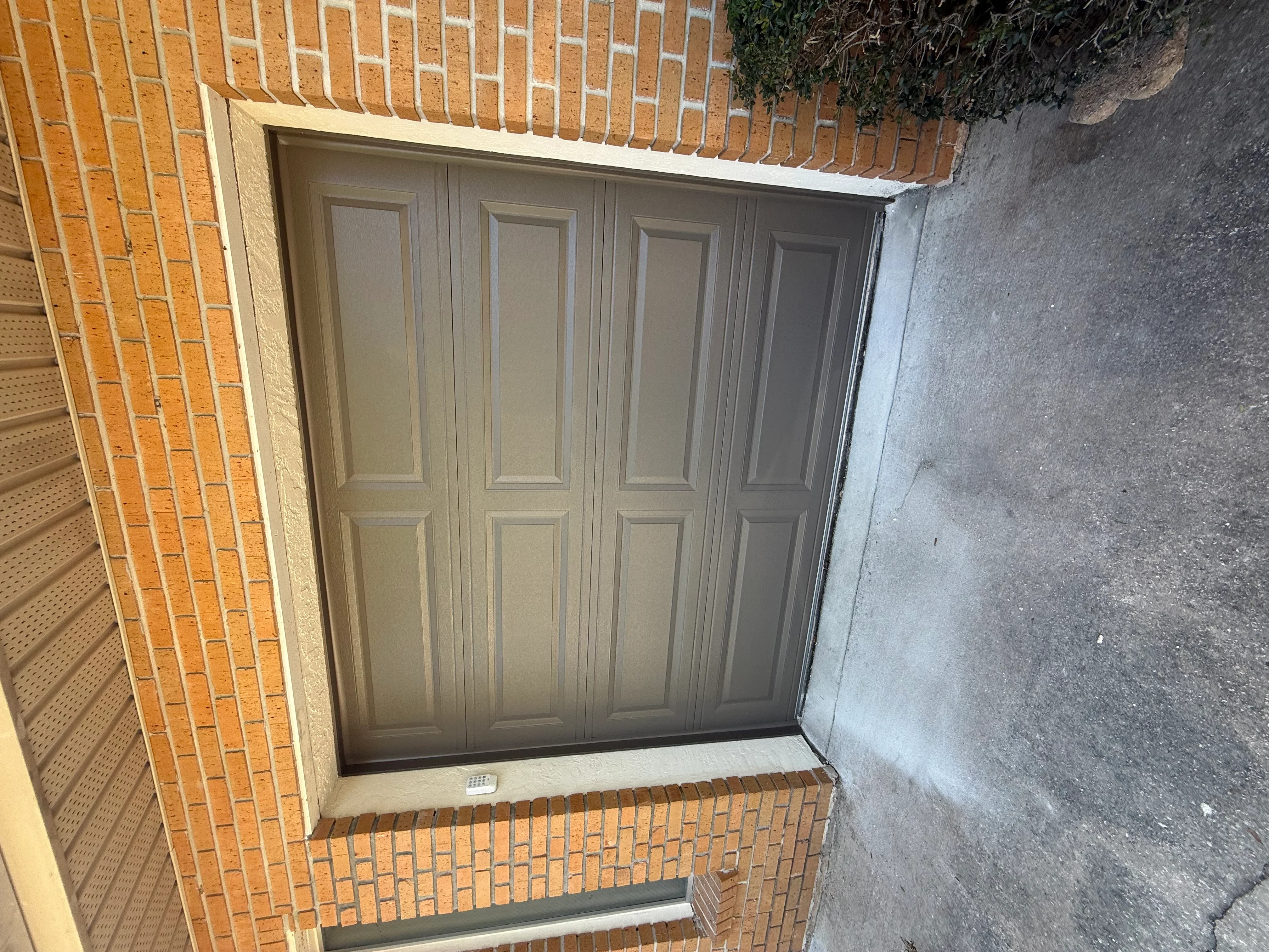 Four-panel tan garage door installed in brick and stucco garage opening