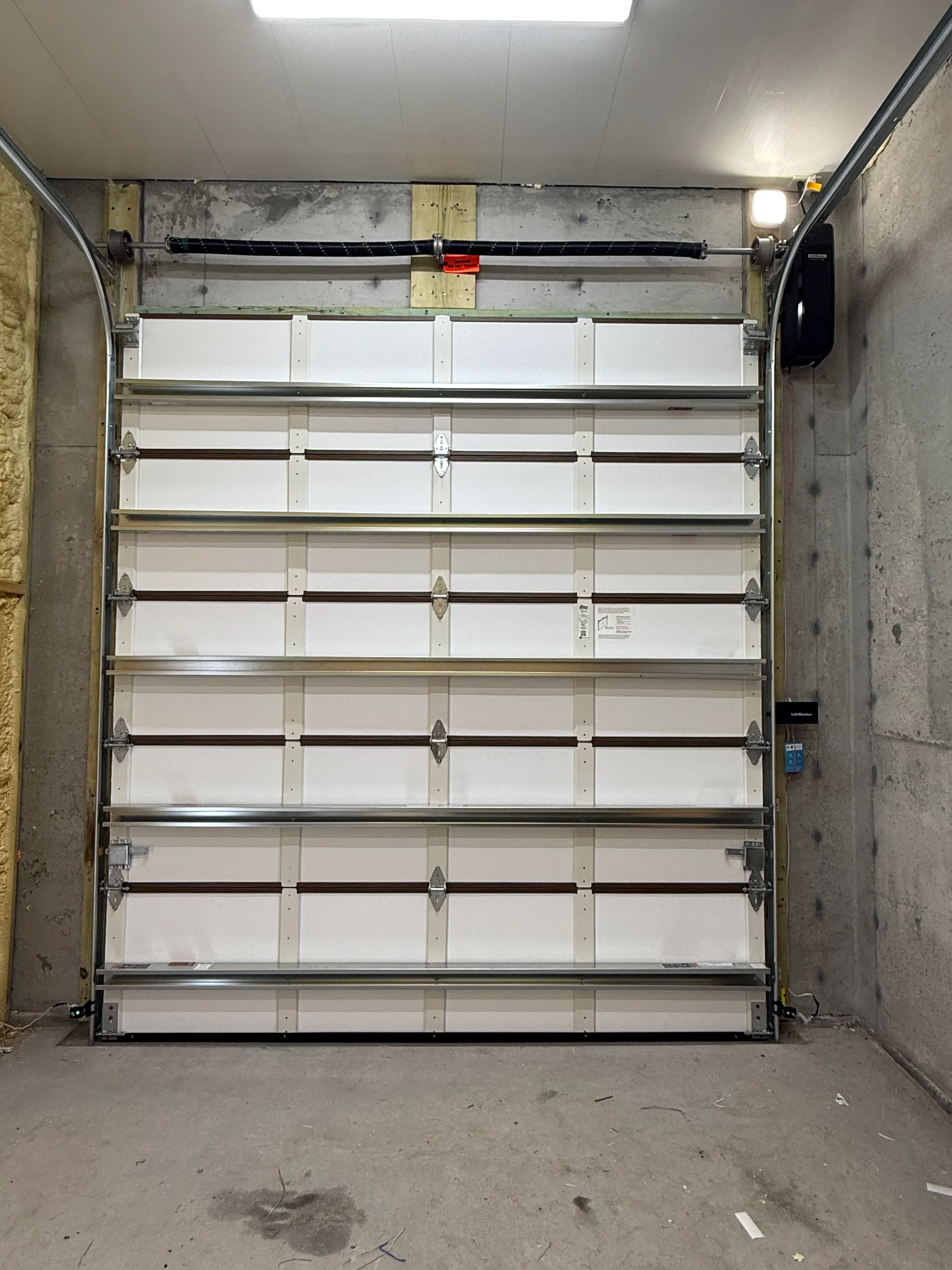 Multi-panel white insulated garage door with aluminum frame and hardware installed in concrete garage opening