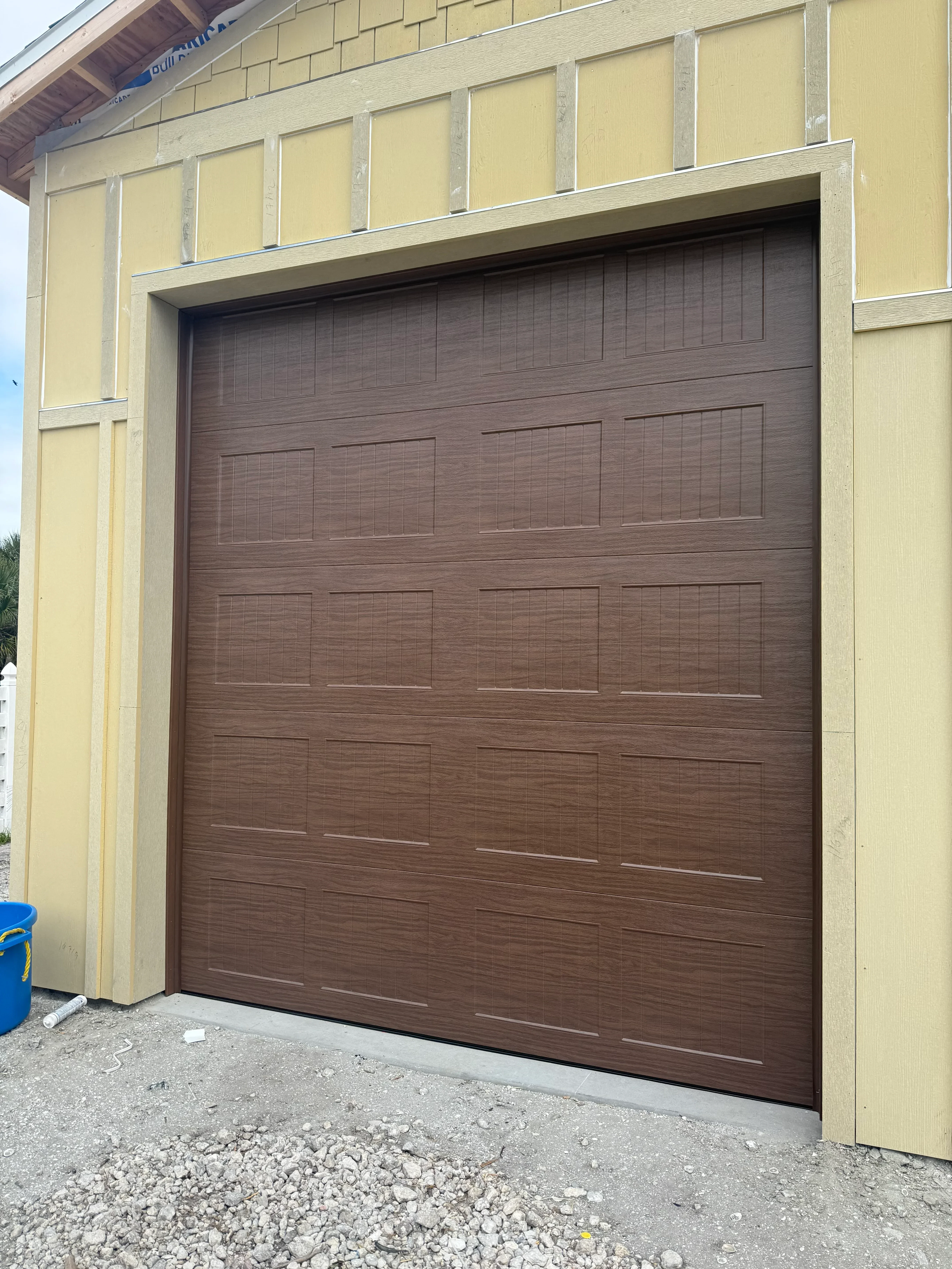 Dark wood-grain garage door with multi-panel recessed design installed in cream frame