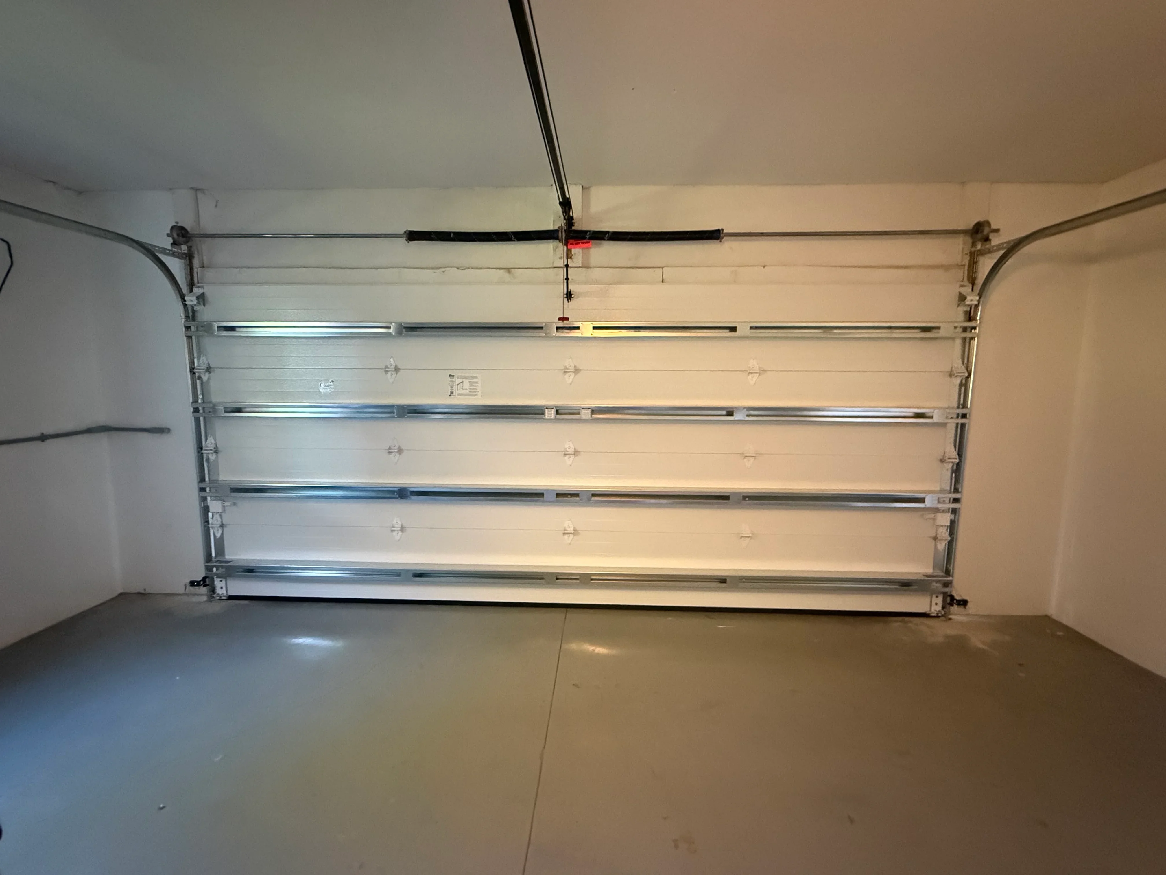 Newly installed white sectional garage door with metal tracks and ceiling-mounted opener system