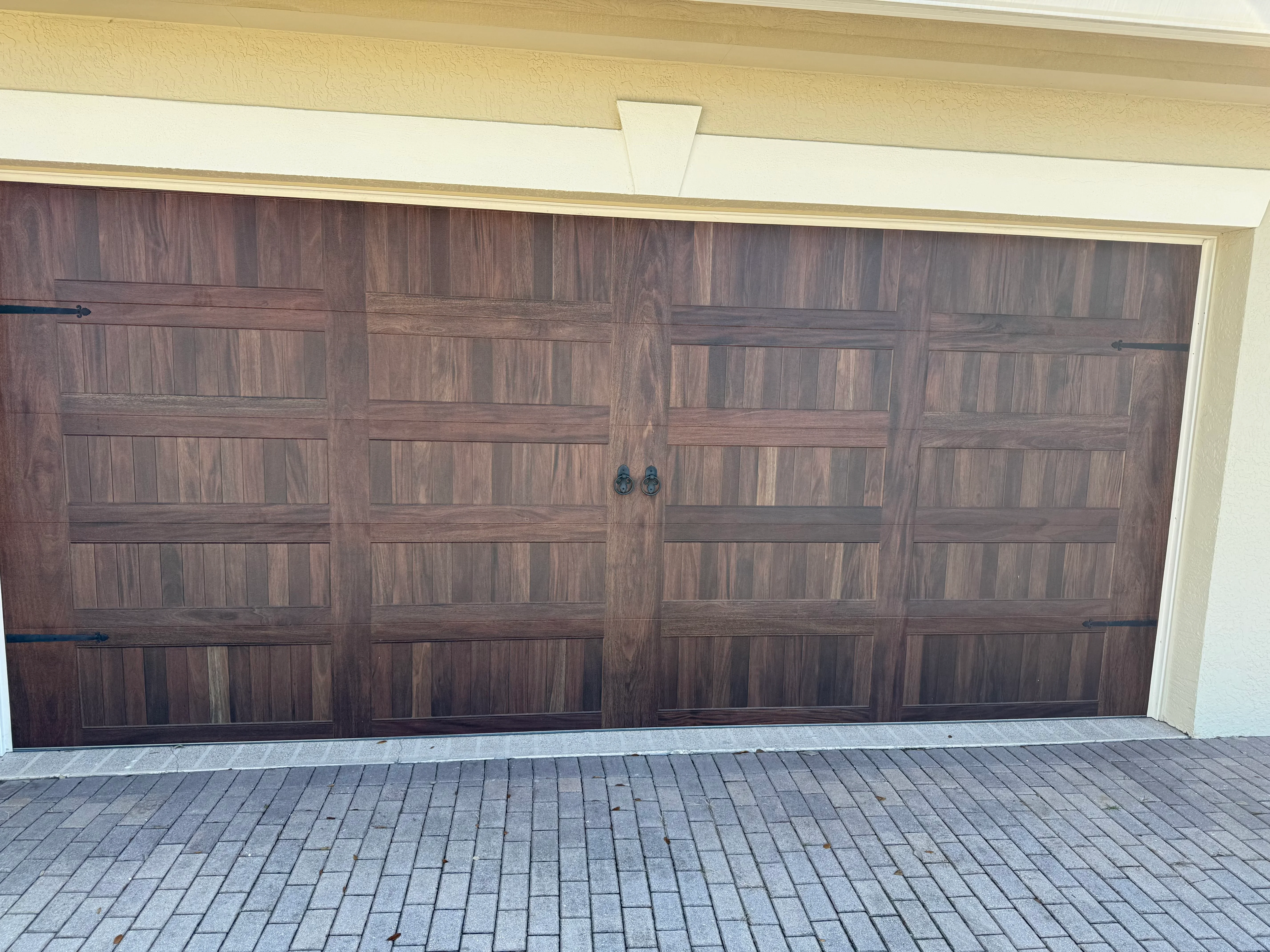 Four-panel wood grain garage door with decorative hardware on cream-colored home