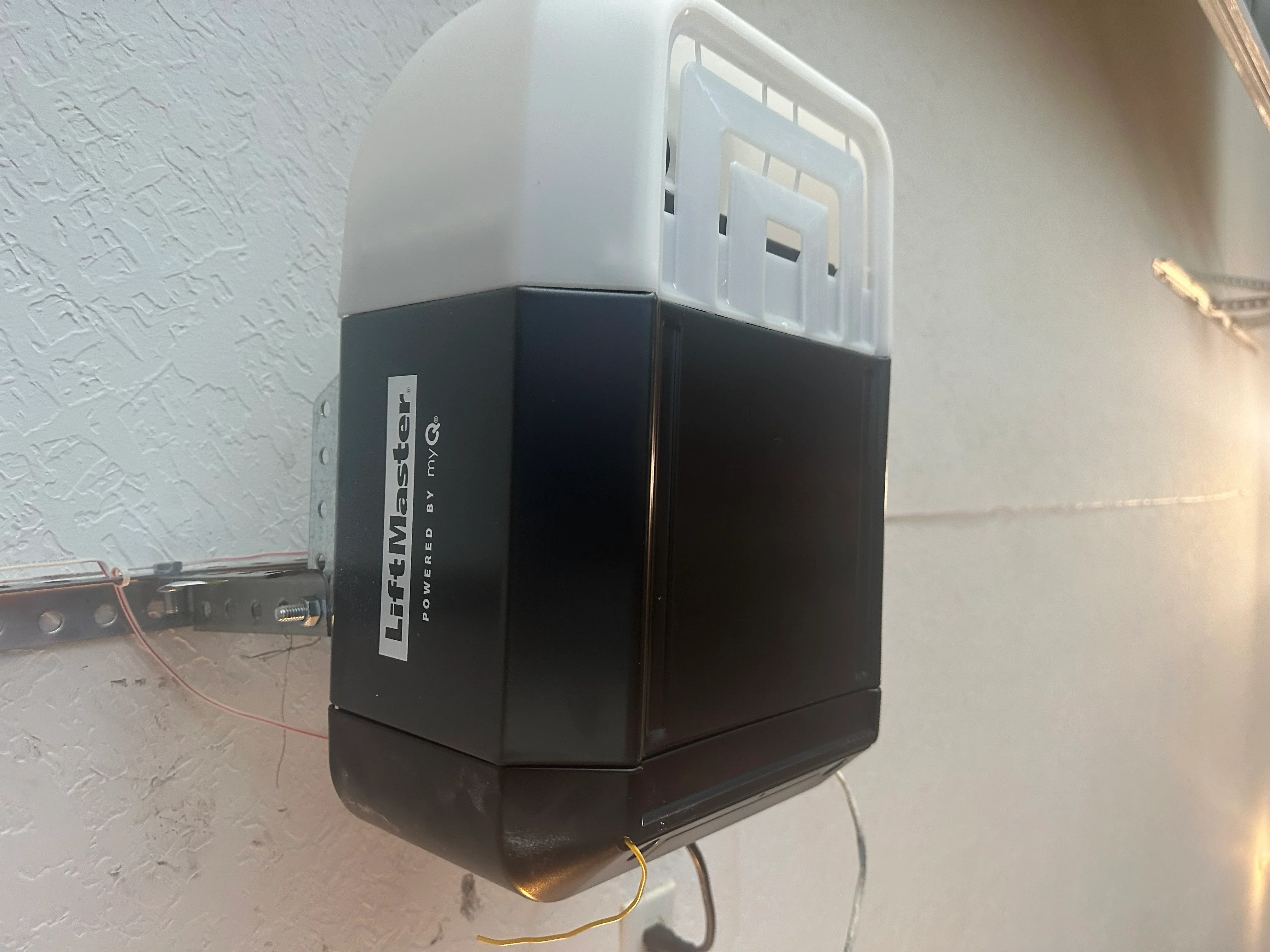 LiftMaster garage door opener installed on white textured wall with black housing and white top unit