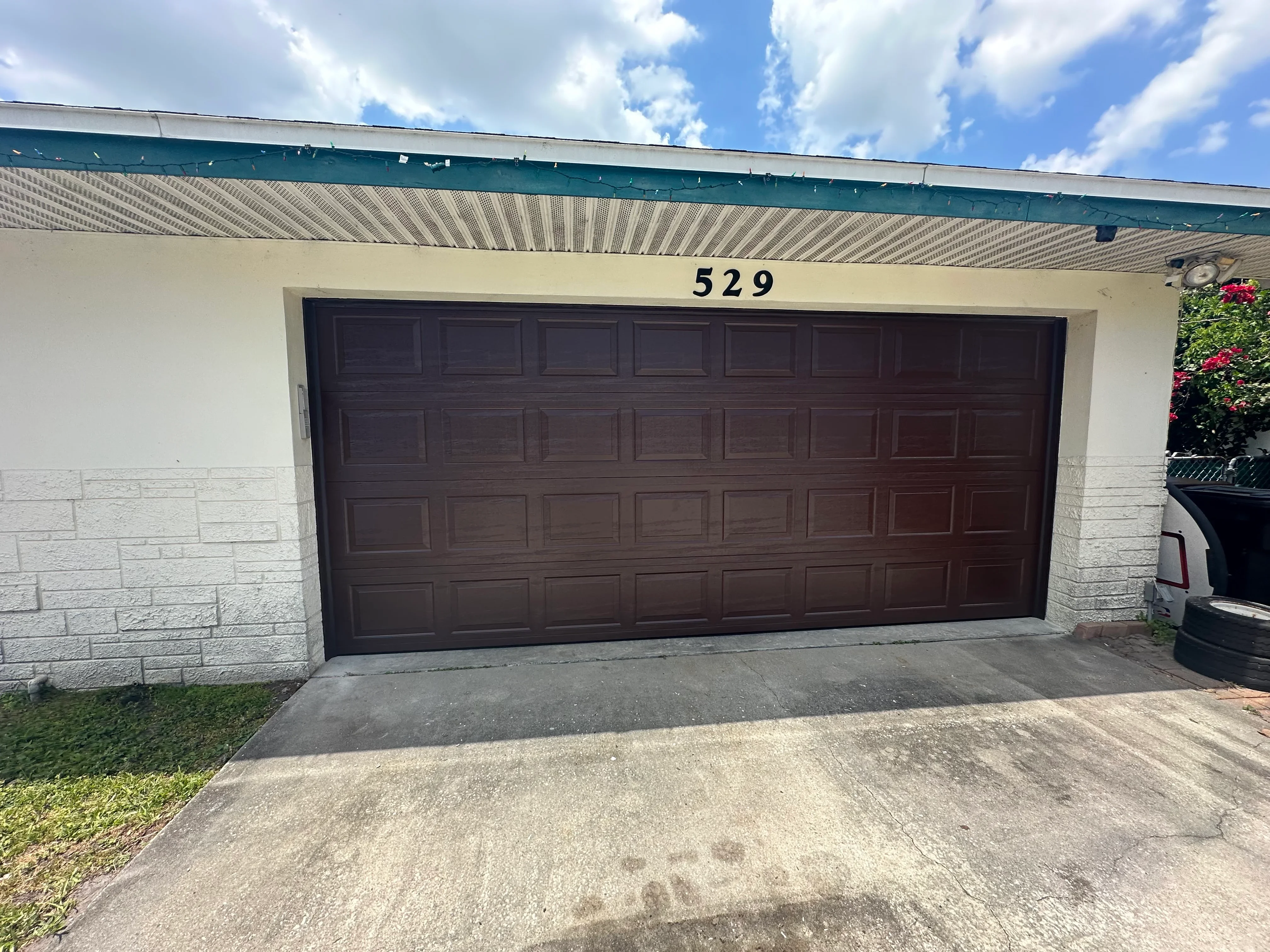 Dark brown multi-panel garage door on white concrete block garage with metal roof