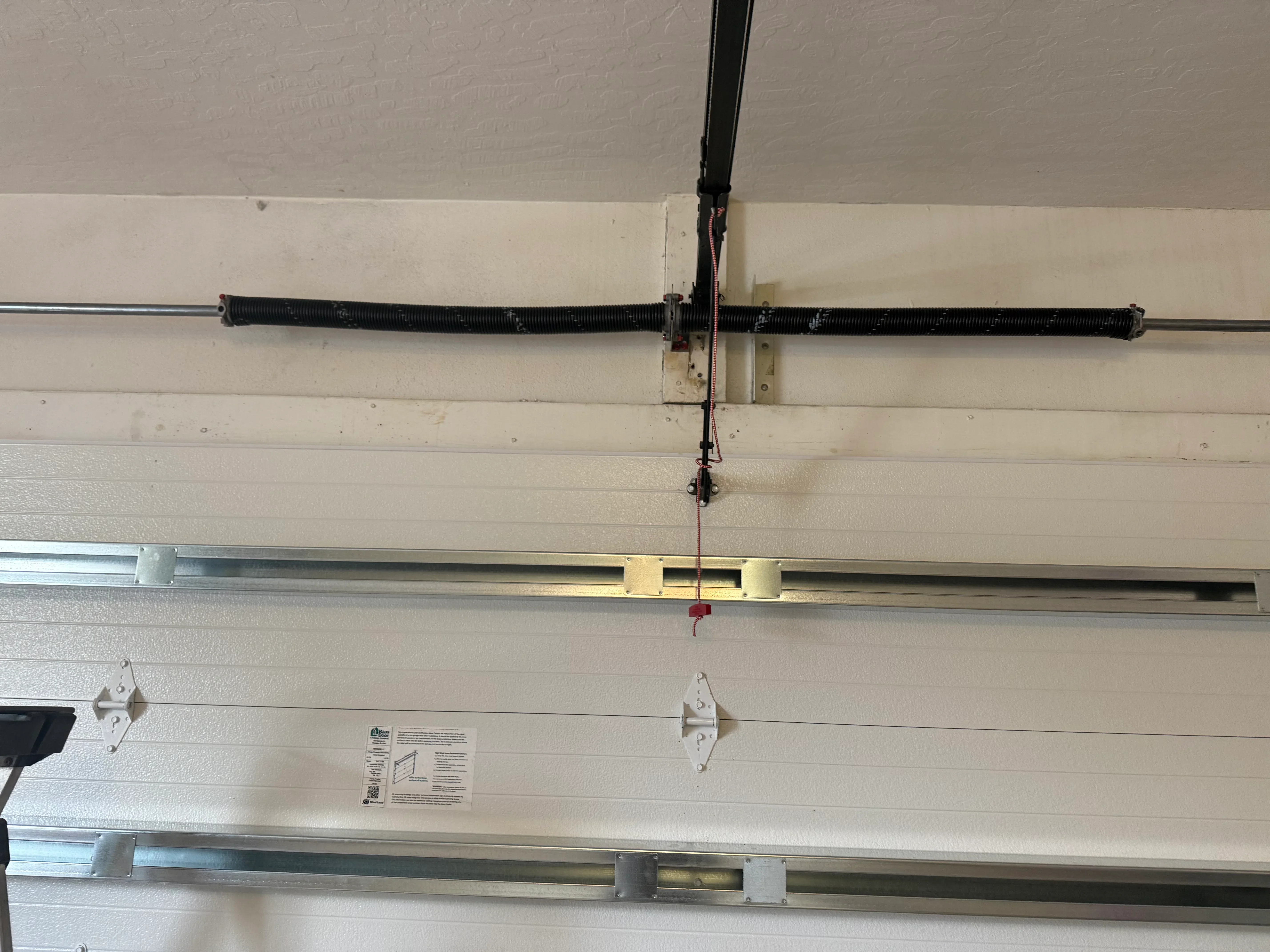 Overhead view of installed garage door spring, cables, and opener hardware on white door